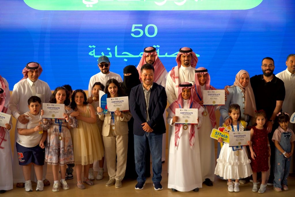 صورة جماعية للمشاركين في مسابقة فايف ون توك للخطابة بالرياض، وندى المغيري تحمل كأس الفوز